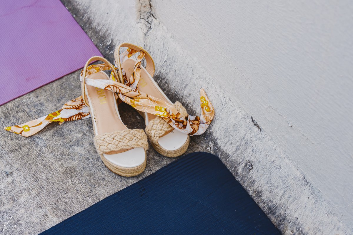 Gold-toned sandals rest beside a softly colored wall.