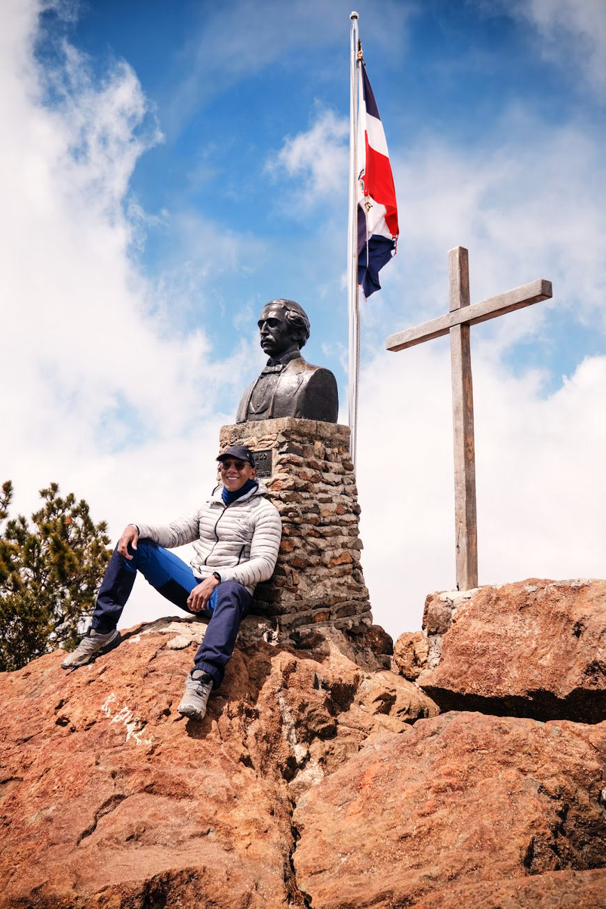 Ricardo seated at the summit beneath the Dominican flag