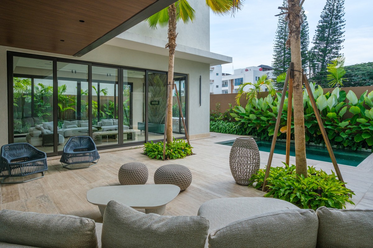 Woven outdoor chairs sit beneath a deep roof beside a tropical garden.