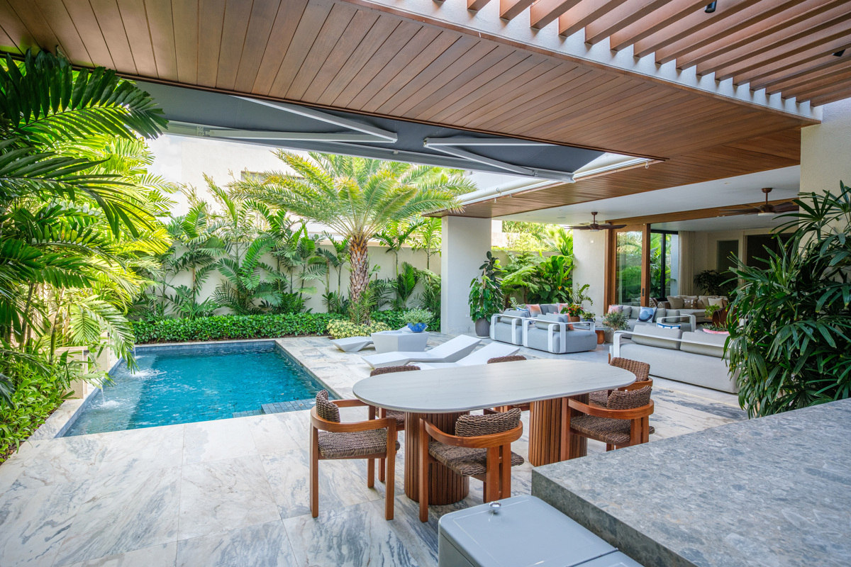 A circular dining table anchors the covered terrace beside the pool.
