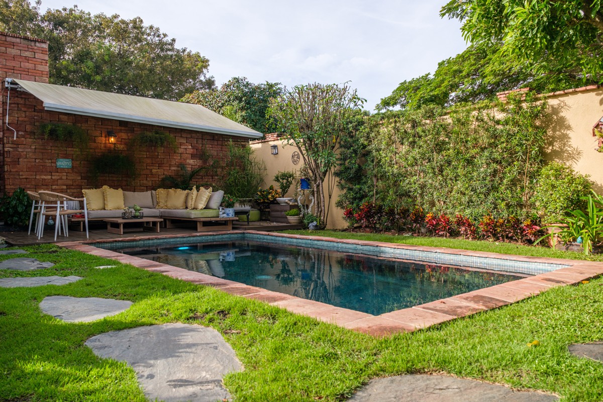 Stepping stones lead across the lawn toward a pool and shaded seating.