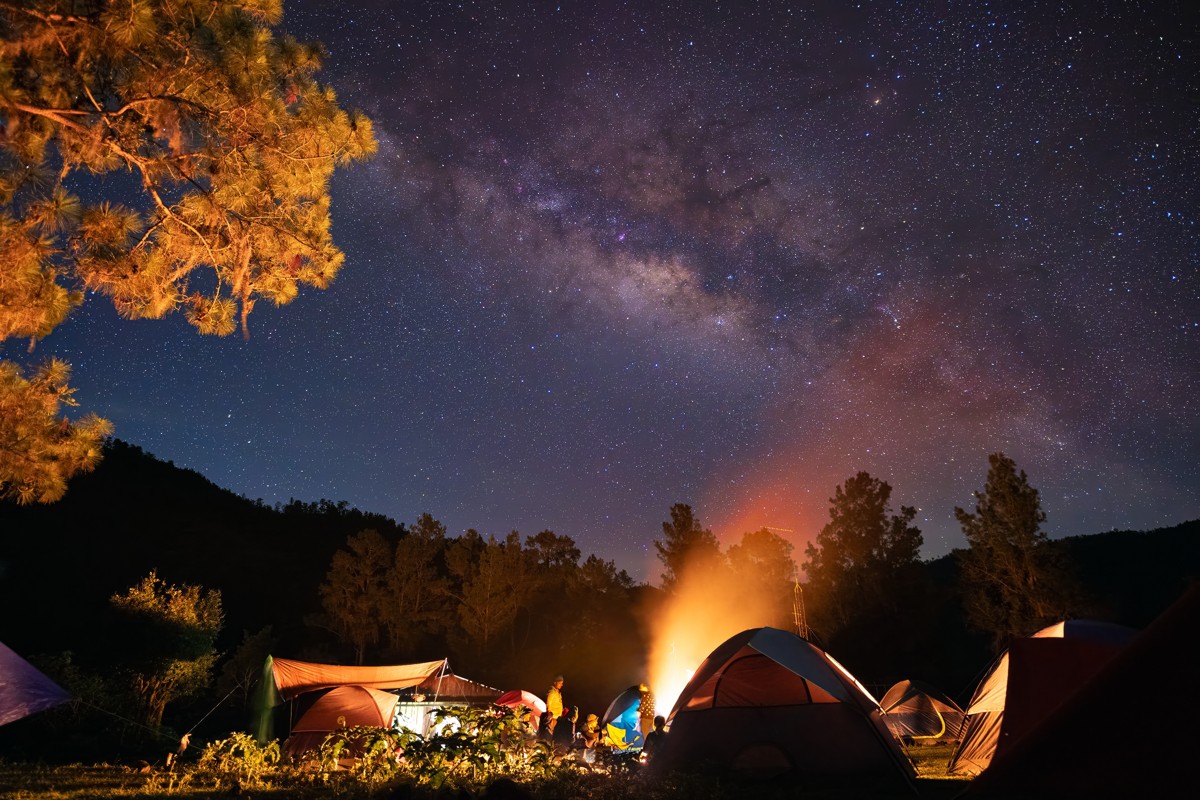 A bright campfire lights tents below the Milky Way.
