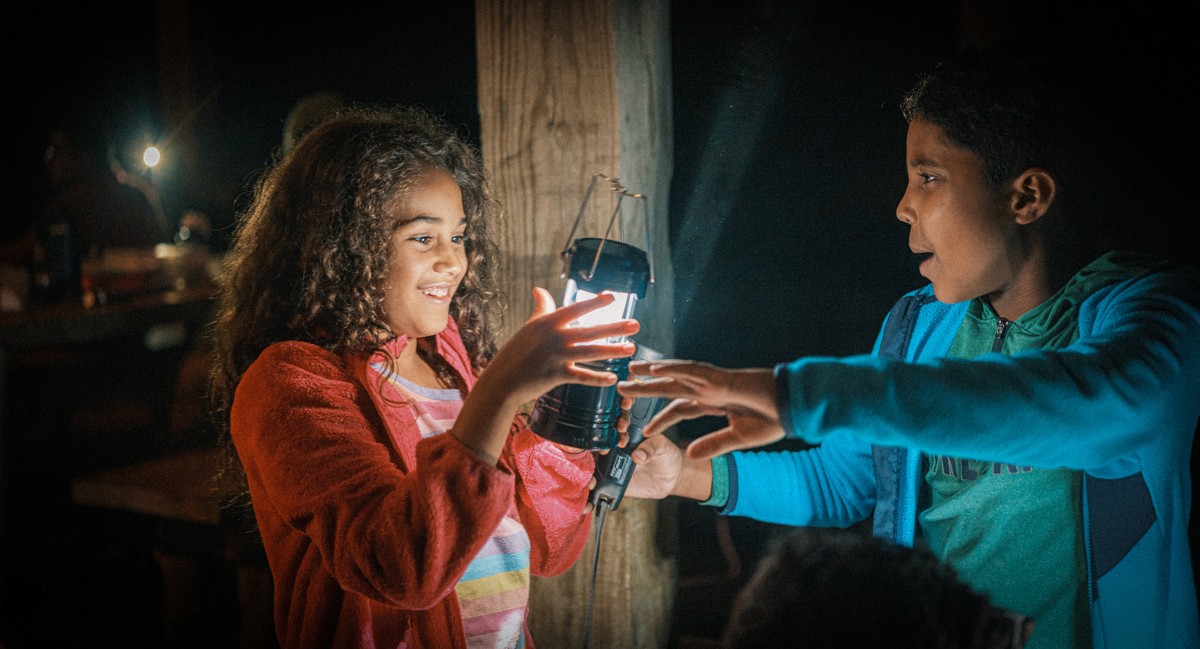 Two people share a brightly lit moment beside a wooden post.