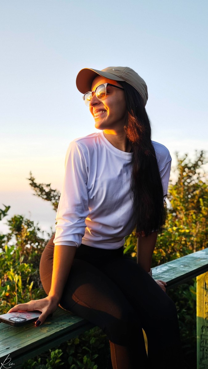 A woman in a cap leans against a railing in warm sunlight.