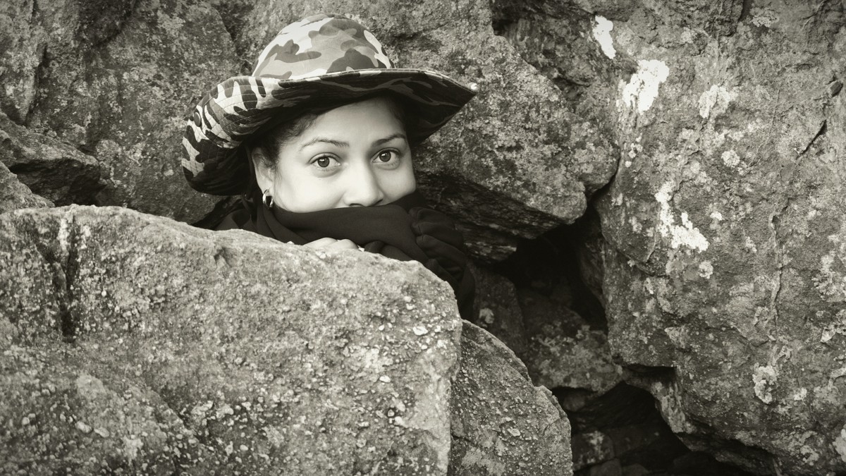 A pair of eyes looks out above a face covering among large rocks.