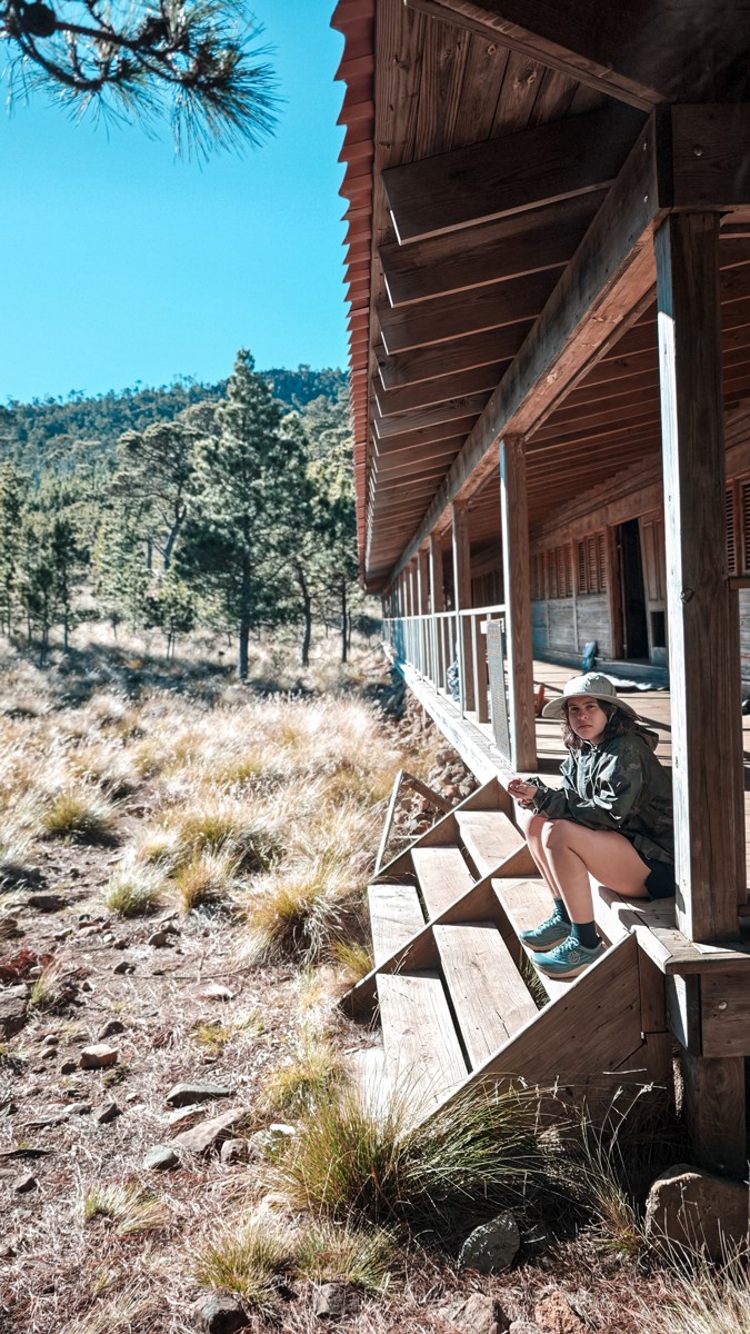 A small figure rests along the shaded side of a timber building.
