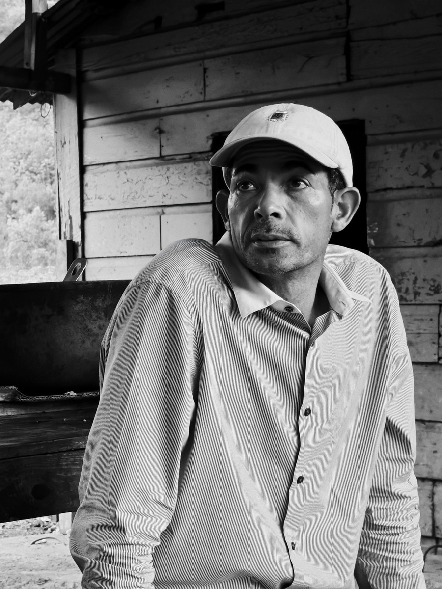 A monochrome portrait frames a man against a wooden wall.