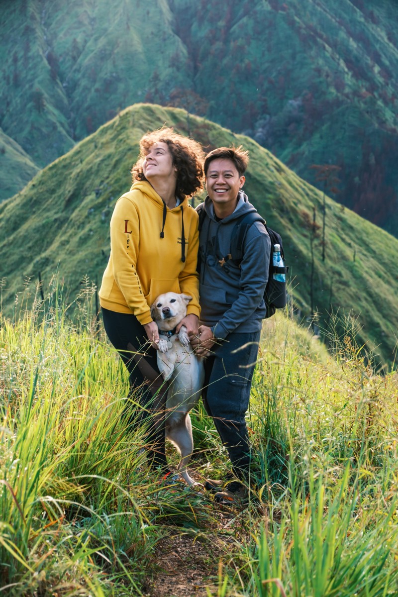 Two hikers pose on a narrow green crest.