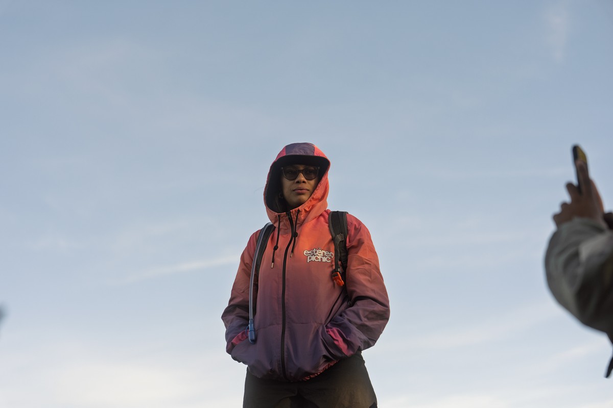 A hooded hiker stands while a phone enters the edge of the frame.