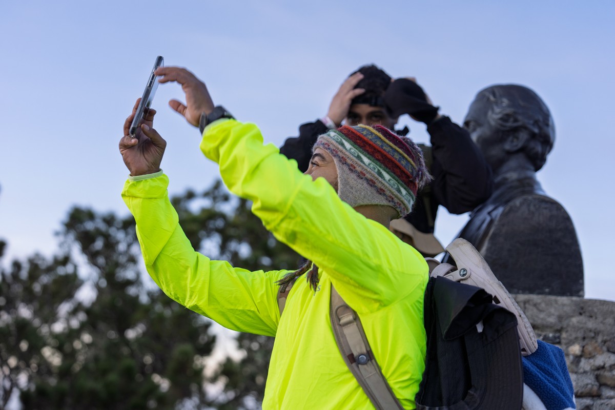 A visitor lifts a phone near a summit monument.
