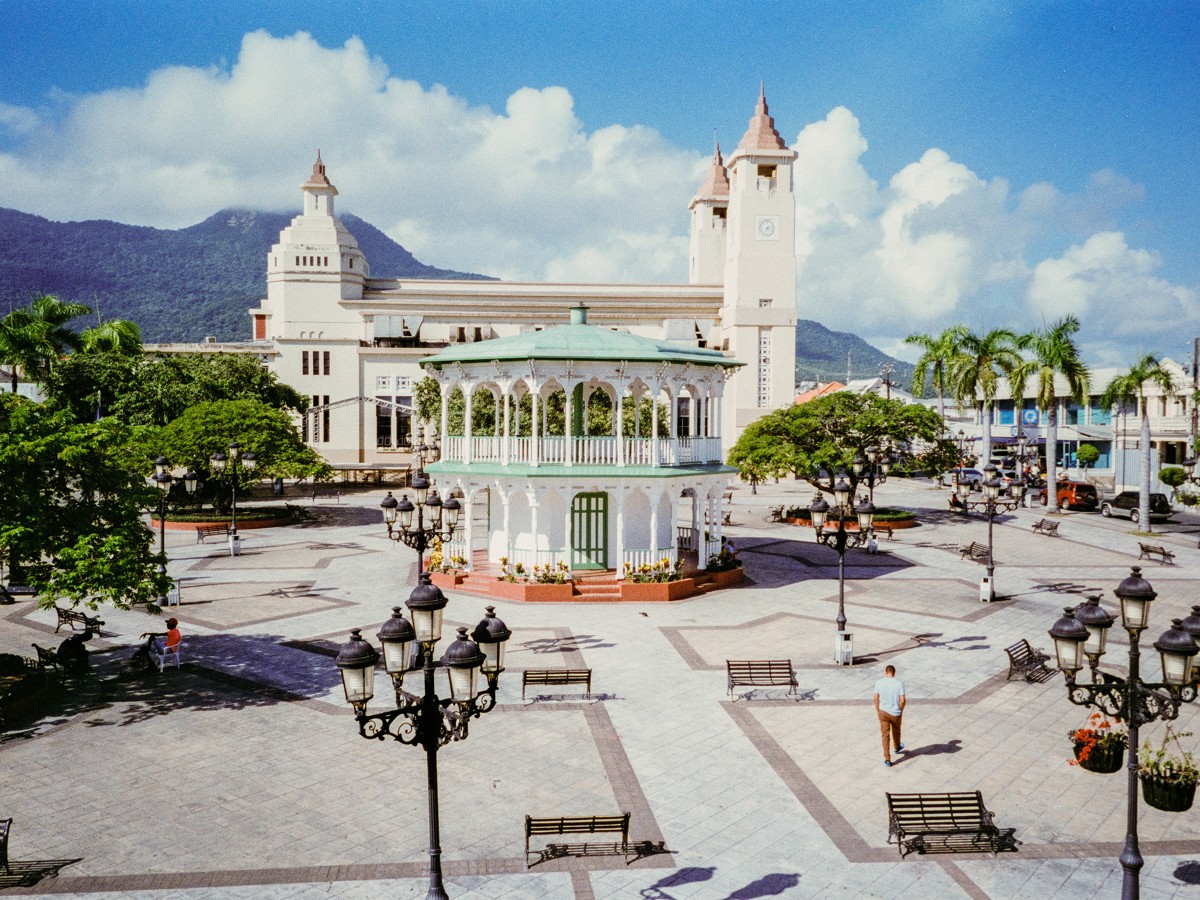 A pale pavilion and civic buildings rise around an open plaza.