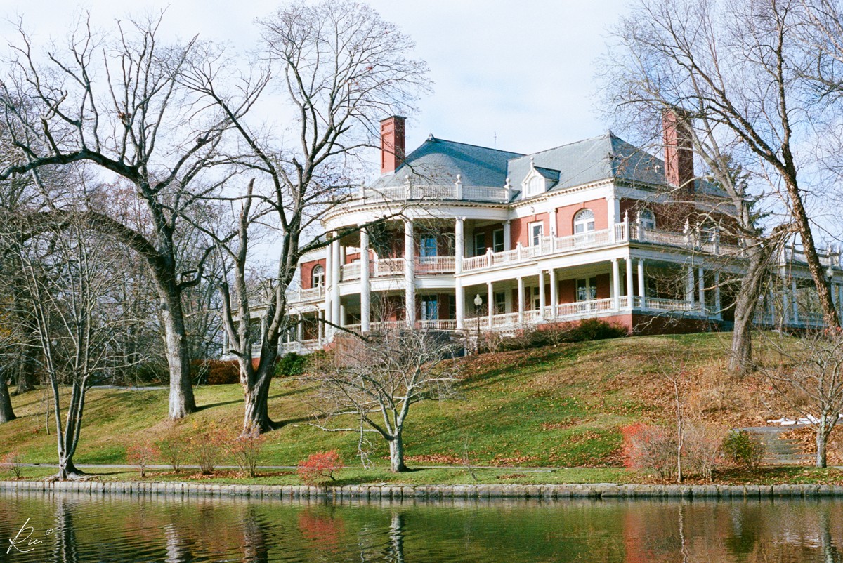 A large veranda-fronted house sits above a quiet pond.