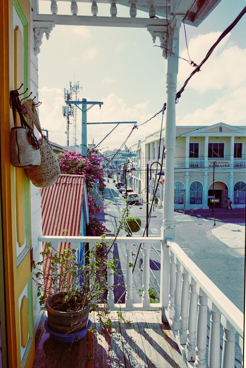 A narrow balcony overlooks colorful buildings and overhead wires.