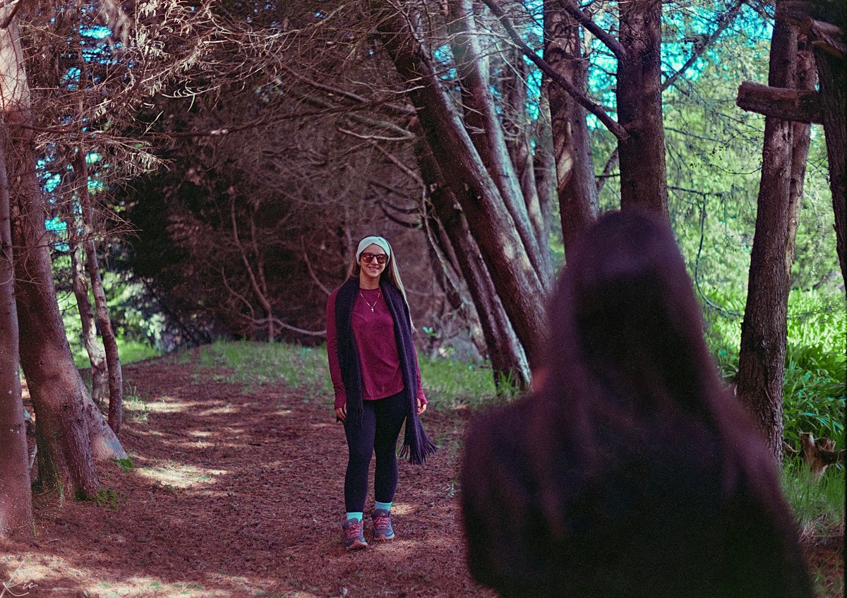 A person stands on a wooded path between large trunks.