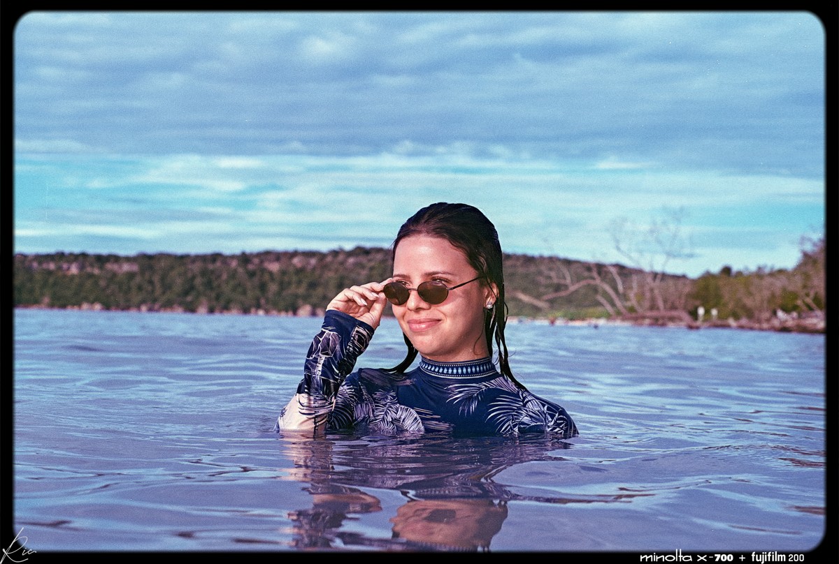 A swimmer in sunglasses turns toward the camera at water level.