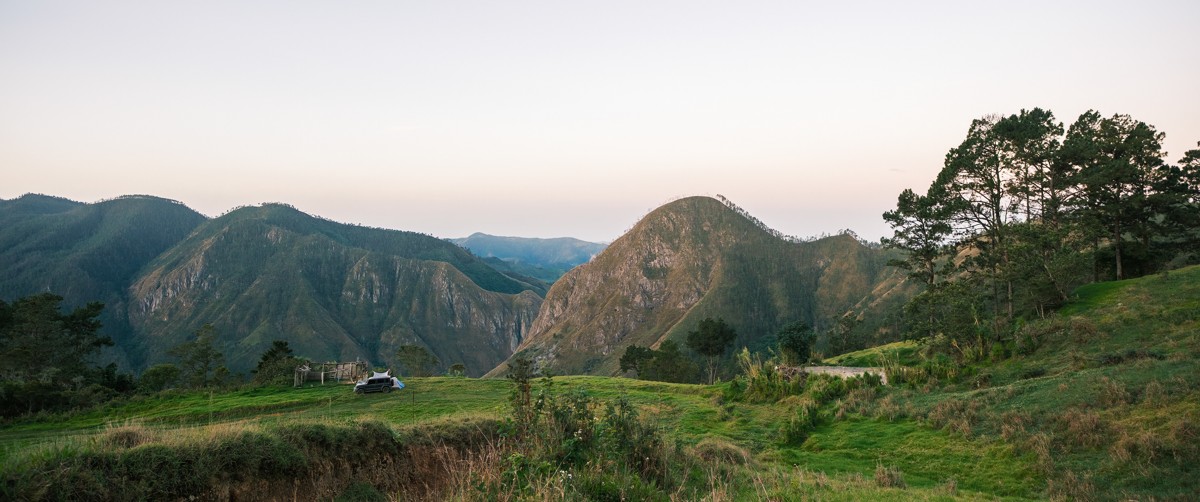 Tents sit low in a wide valley enclosed by green mountains.