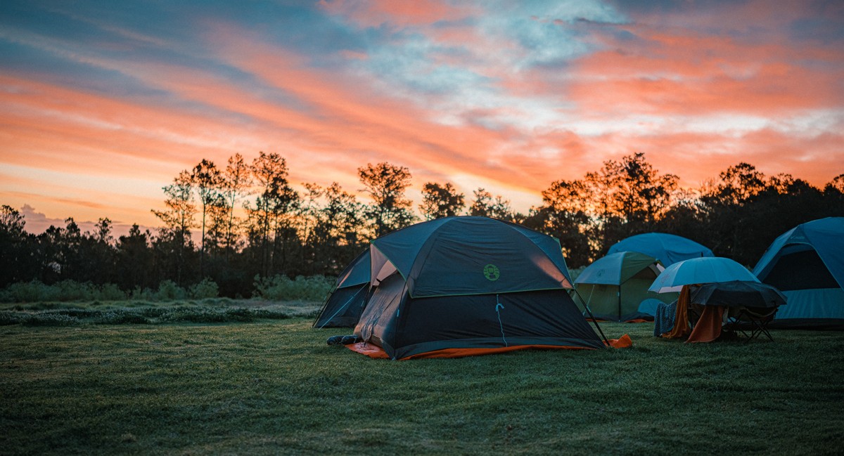 Orange clouds stretch over tents pitched on open grass.