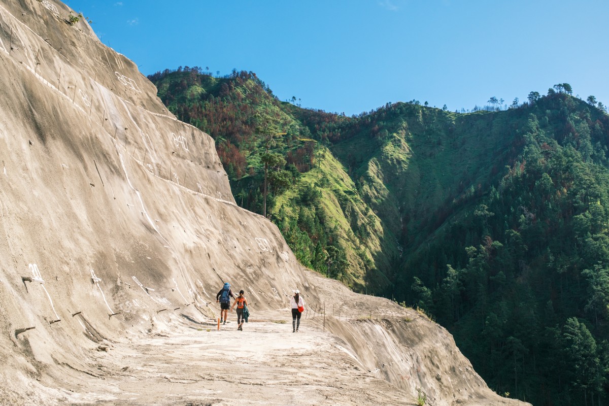 Walkers appear small below a broad sloping wall of stone.