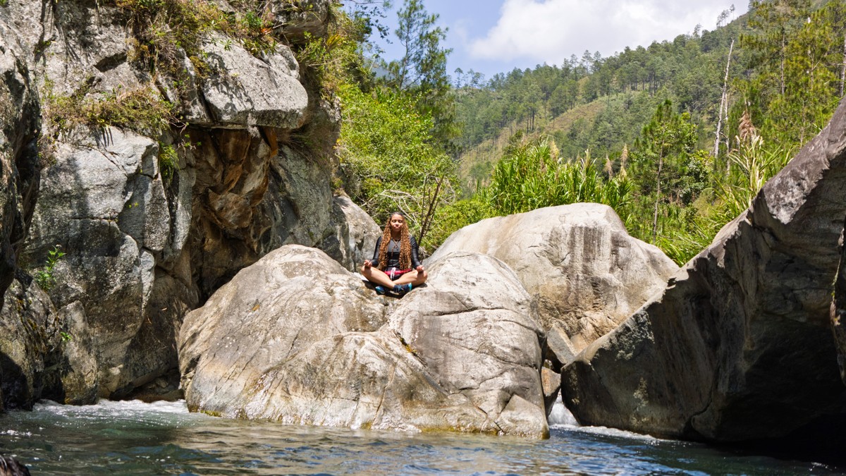 A person rests among pale rocks beside flowing water.