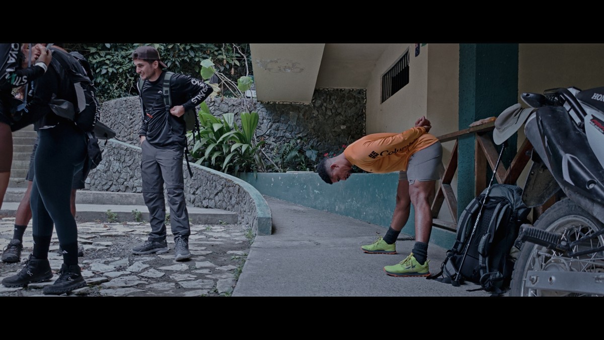 Hikers gather with packs and stretch beside a building.