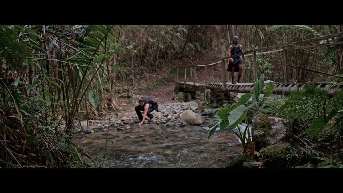 Hikers pause by a rocky stream beside a footbridge.