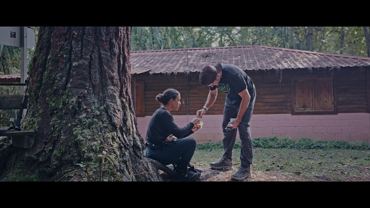 Two people attend to something beside a large tree and cabin.