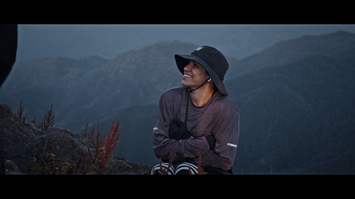 A seated hiker looks upward against the mountain backdrop.