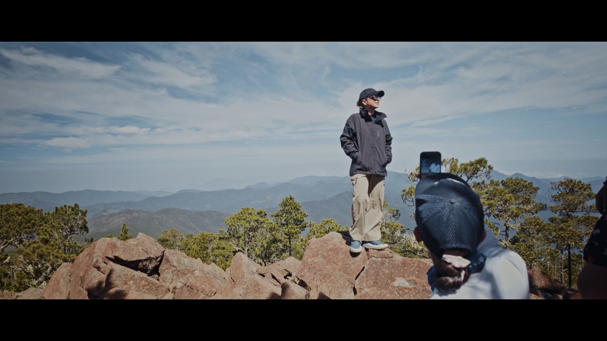 Hikers occupy a rocky summit beneath an open blue sky.