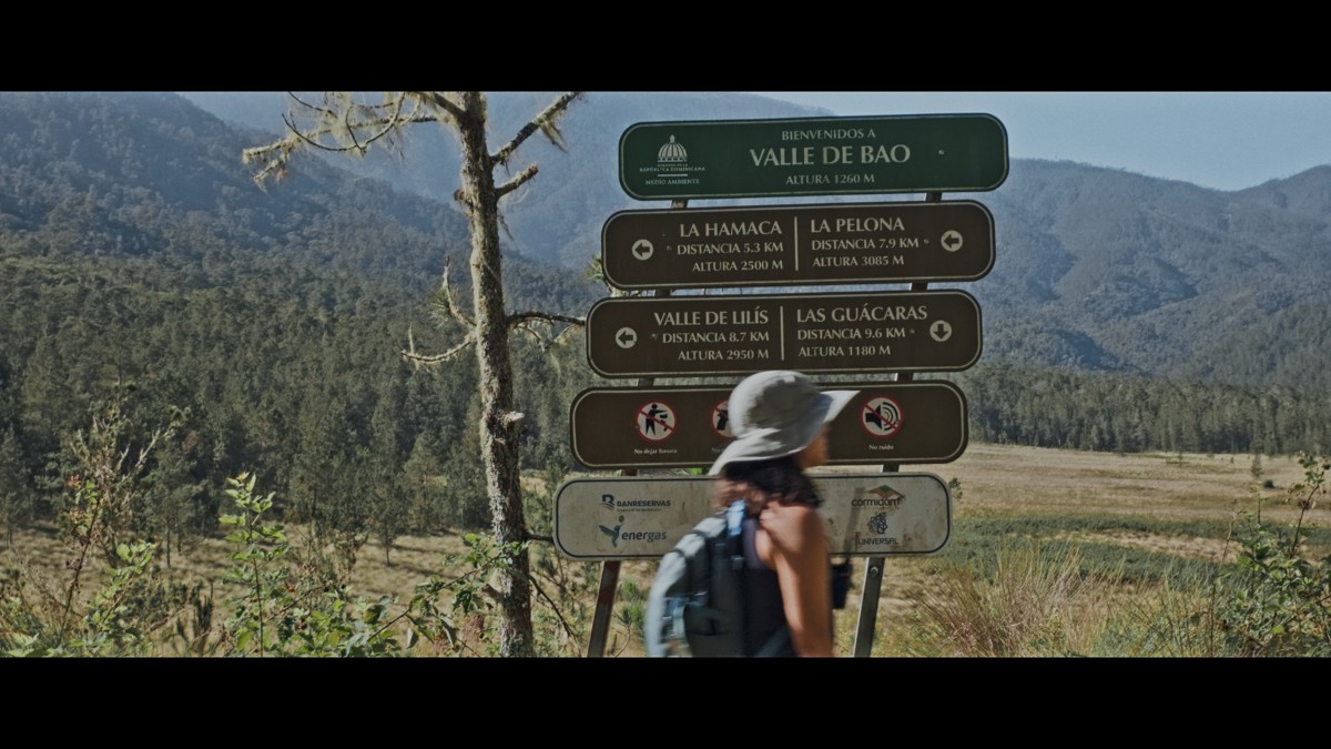 A hiker passes a stack of trail signs above the valley.