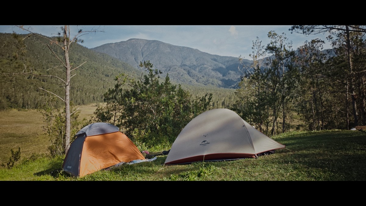 Two tents face the mountains from a grassy clearing.