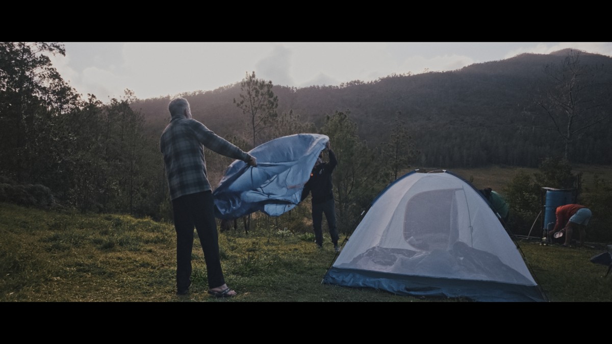 A camper spreads fabric beside a small tent.