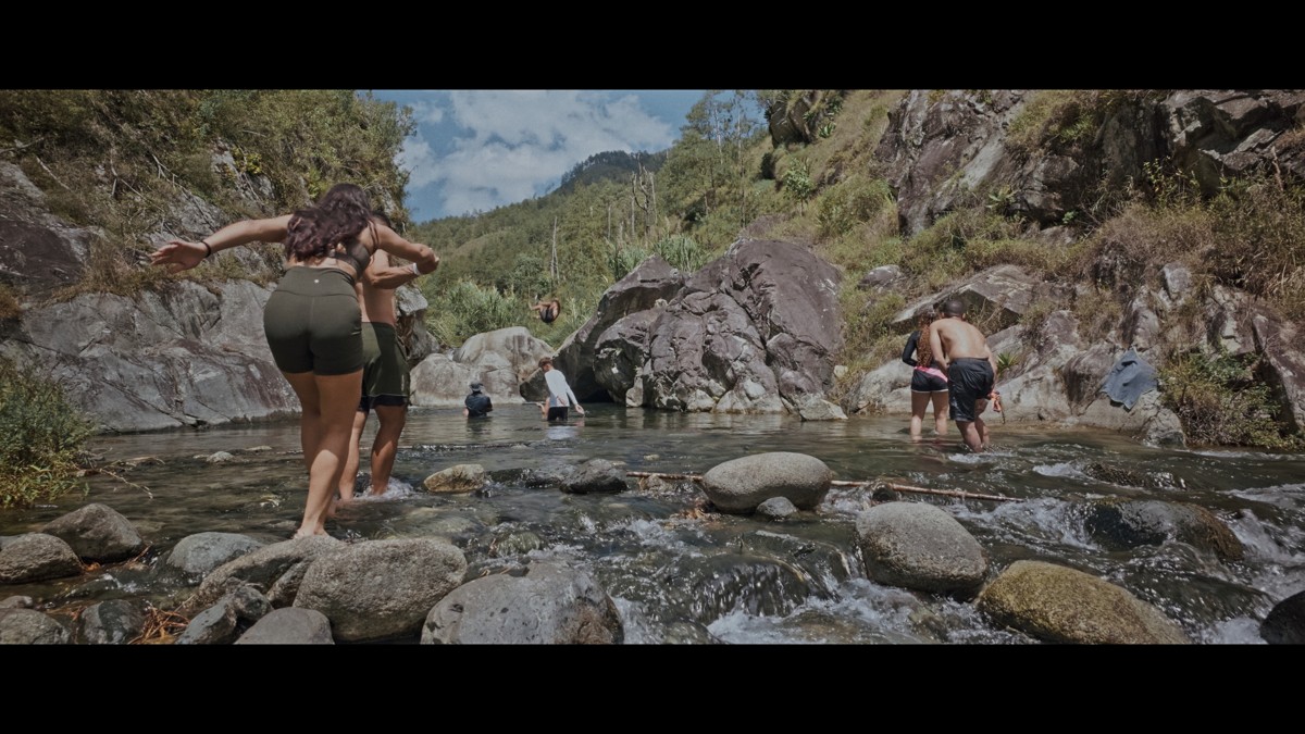 Hikers negotiate stones at a shallow river crossing.