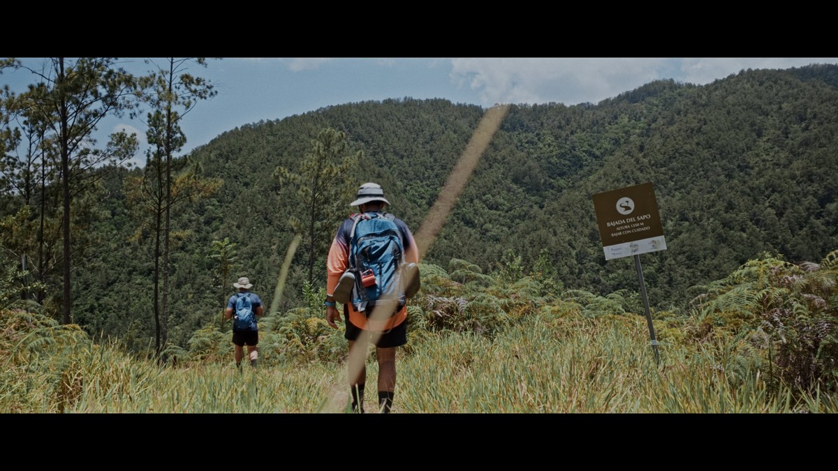 A backpacker follows the path toward a green mountain wall.