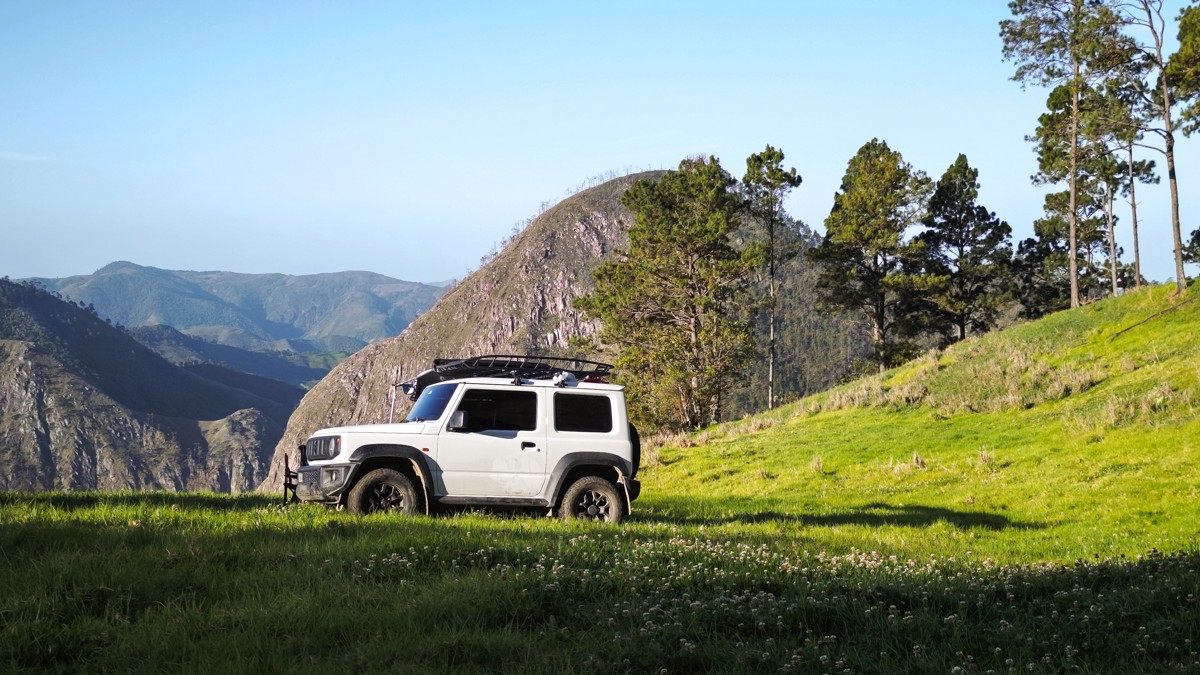 A white off-roader rests on grass against steep mountain slopes.