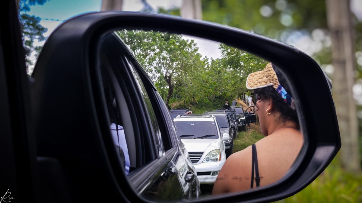 A side mirror frames a passenger and the vehicles following.