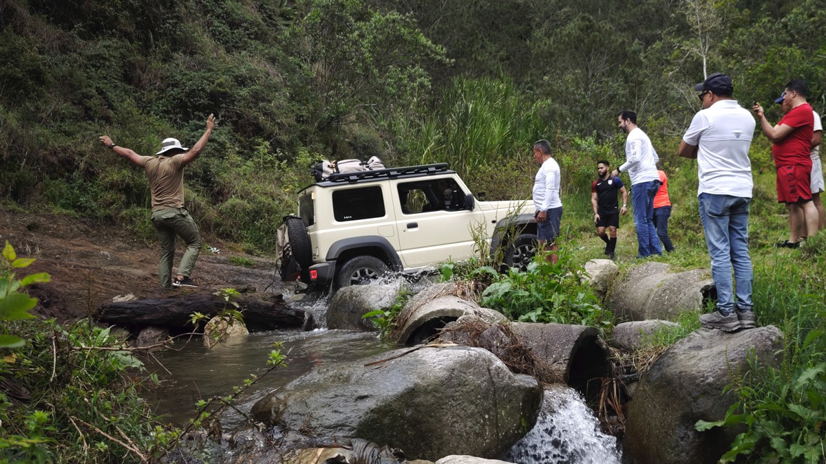 People stand beside a white vehicle negotiating a rocky stream.