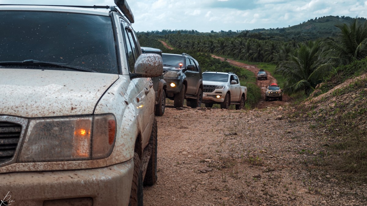A line of vehicles stretches back along a rough open road.
