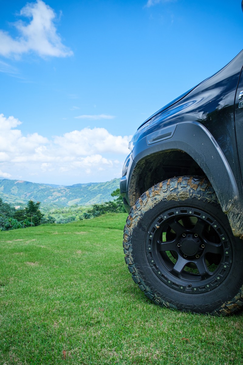 A low view pairs a vehicle wheel with grass and distant hills.